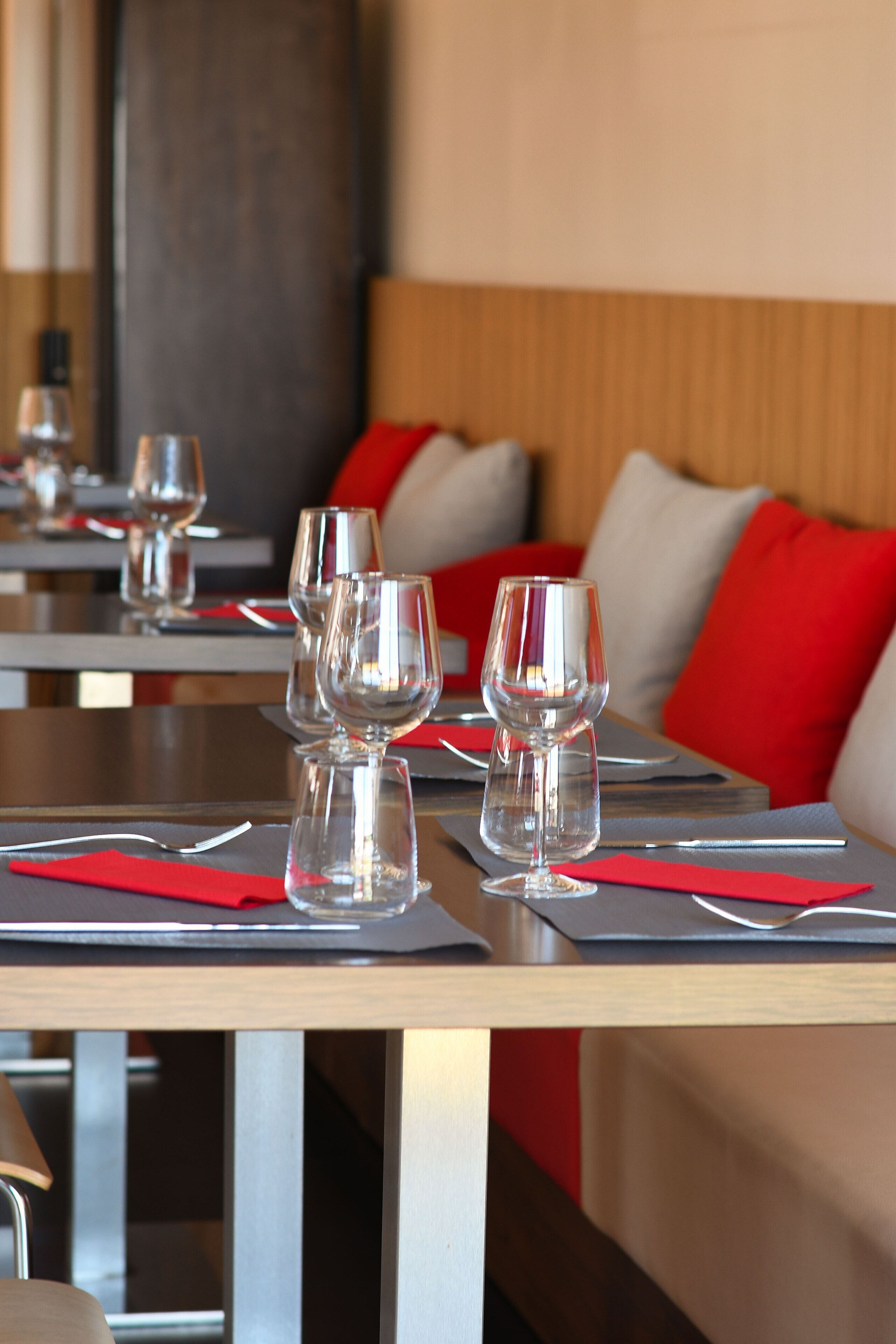 A restaurant setting with tables set for dining, featuring red napkins and clear glassware.
