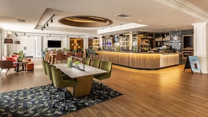 A modern hotel lobby with a bar area, seating arrangements, and a large television screen.