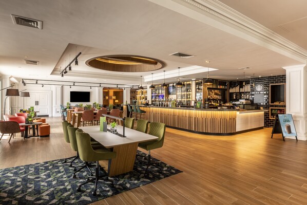 A modern hotel lobby with a bar area, seating arrangements, and a large television screen. - Holiday Inn Guildford by IHG (Guildford)