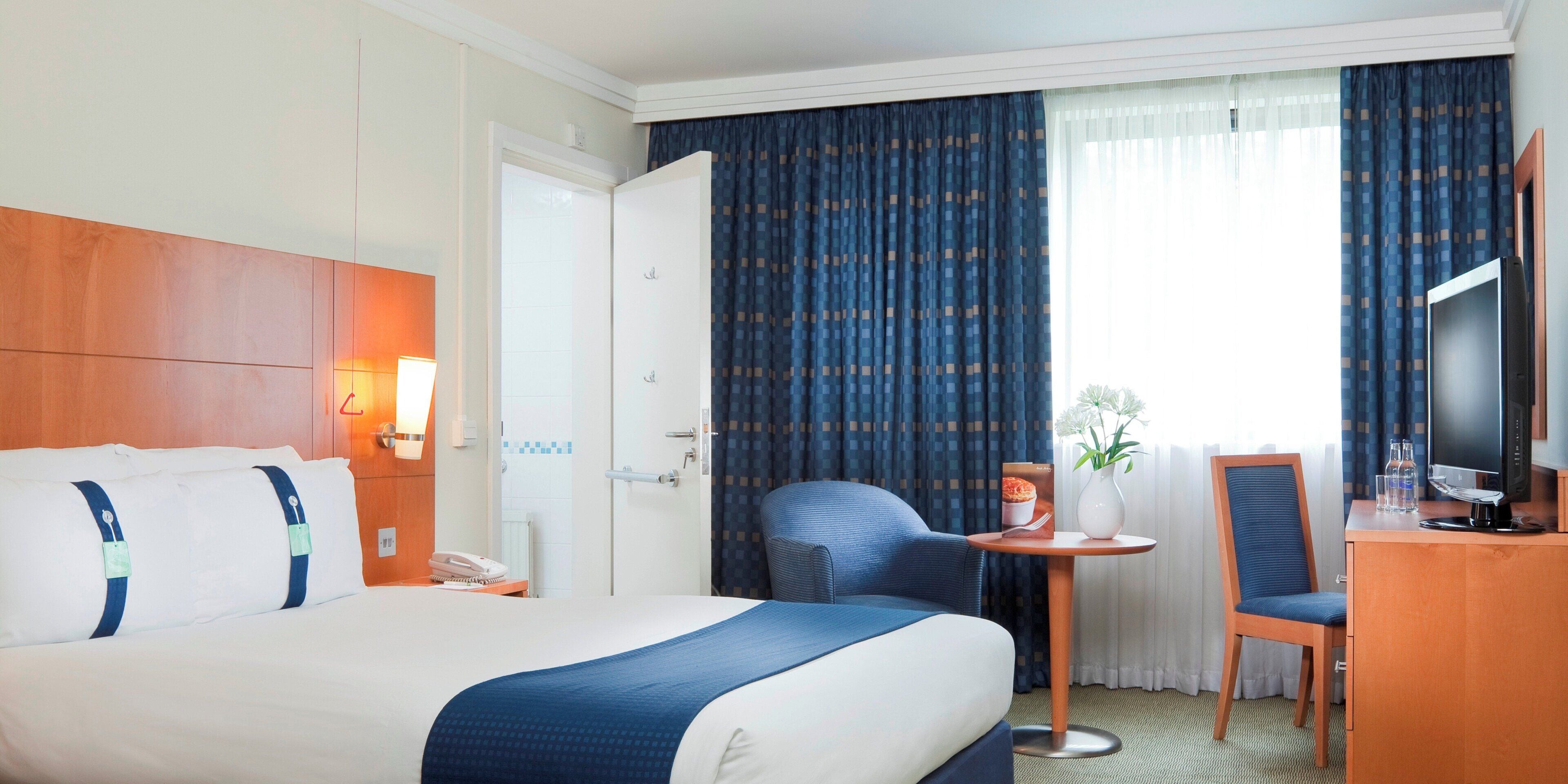 A hotel room with a bed, a desk with a chair, a television, and a window with curtains.