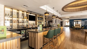 A bar area with wooden bar counters, green bar stools, and a variety of bottles and glasses.
