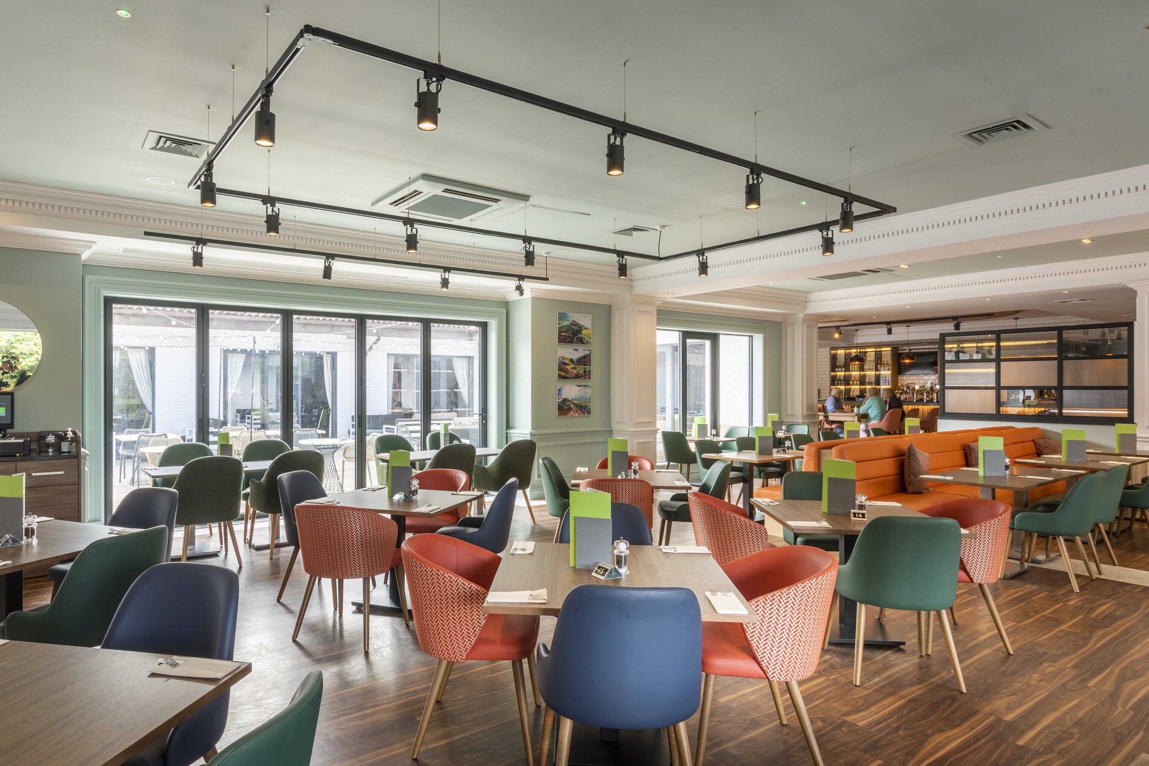 A spacious dining area with multiple tables and chairs, large windows, and a bar area with seating.