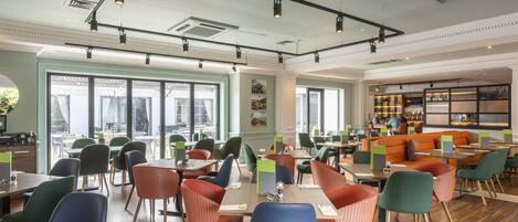 A spacious dining area with multiple tables and chairs, large windows, and a bar area with seating.