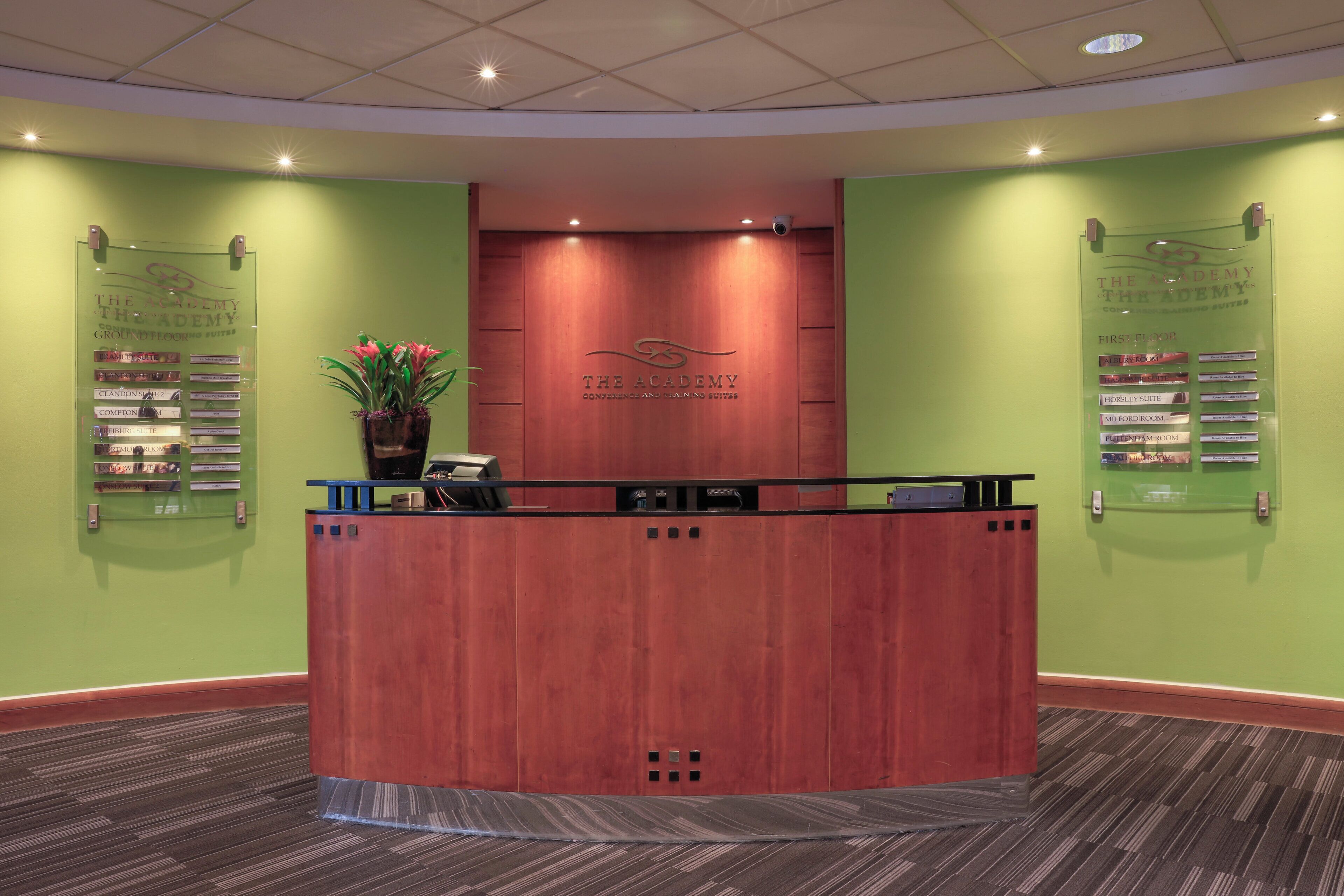 A reception desk with a wooden finish, a potted plant, and a sign listing conference and banquet suites.
