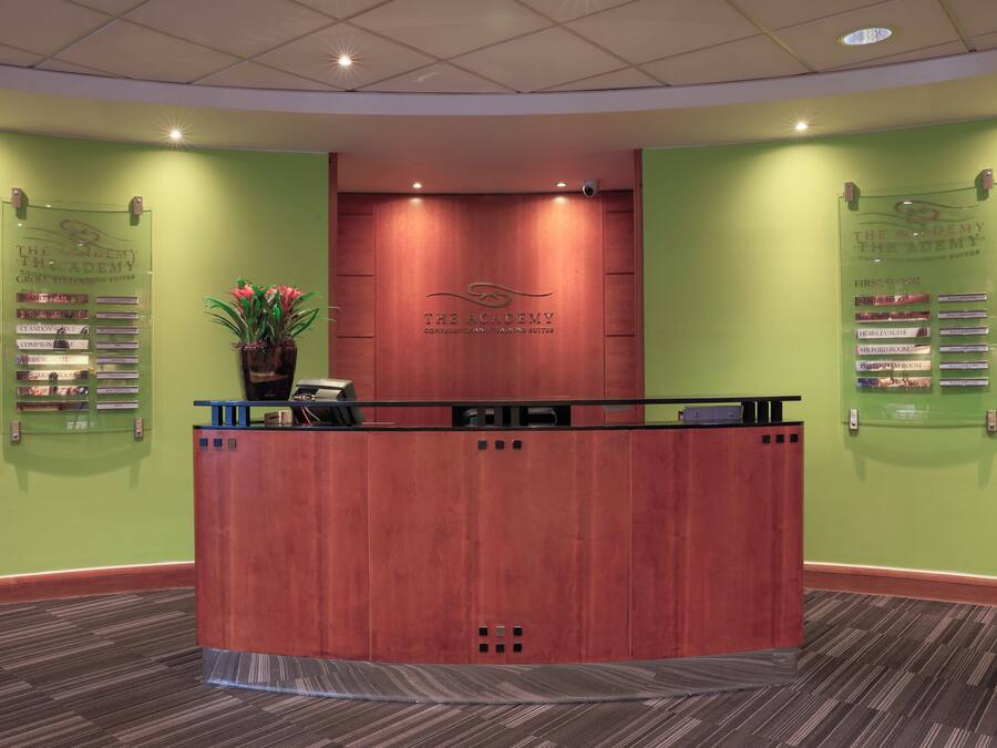 A reception desk with a wooden finish, a potted plant, and a sign listing conference and banquet suites.