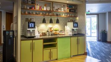 Une cuisine moderne équipée d’une machine à café, d’un réfrigérateur, ainsi que de divers pots et récipients rangés sur des étagères.