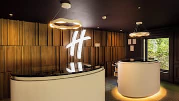 Two reception desks with black tops sit against a backdrop of paneling, surrounded by pendant lights and a geometric tile floor.