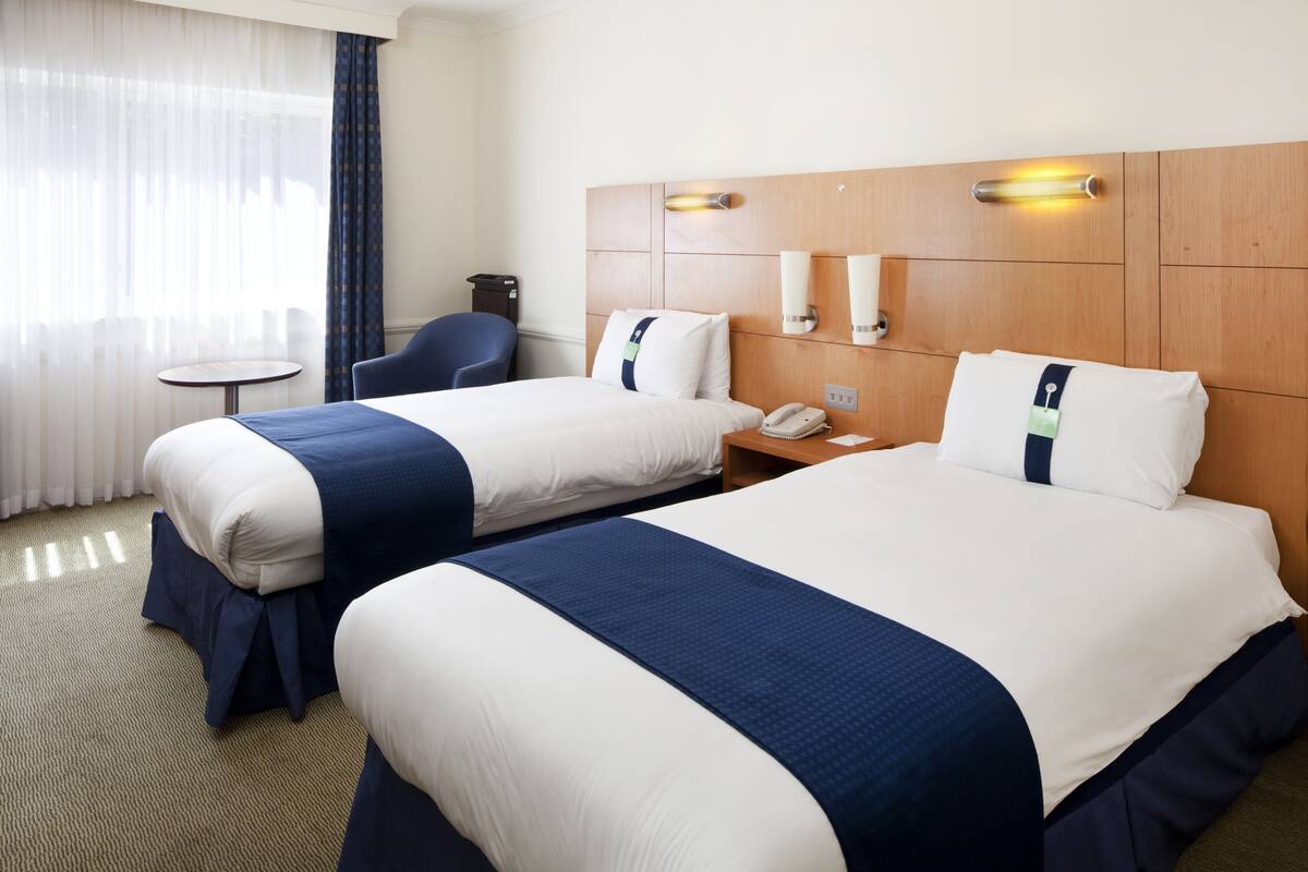 A hotel room with two beds, a small table, a chair, and a nightstand with a phone.
