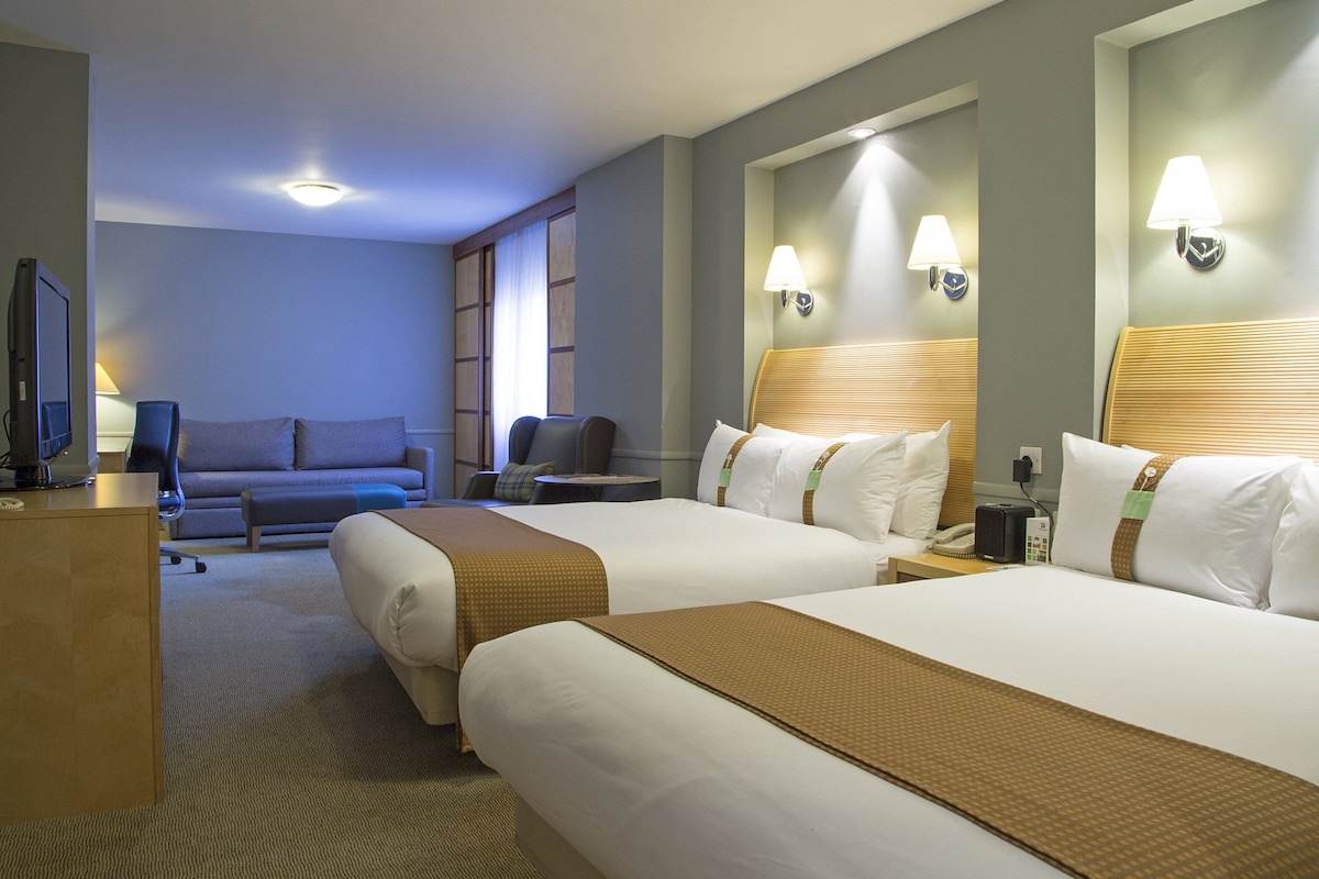 A hotel room with two beds, a desk, a television, a sofa, and a lamp.