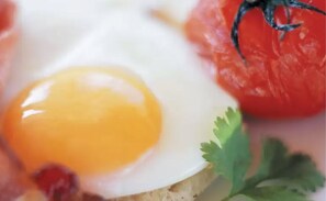 A close-up of a fried egg on a slice of bread with a tomato and a sprig of cilantro.