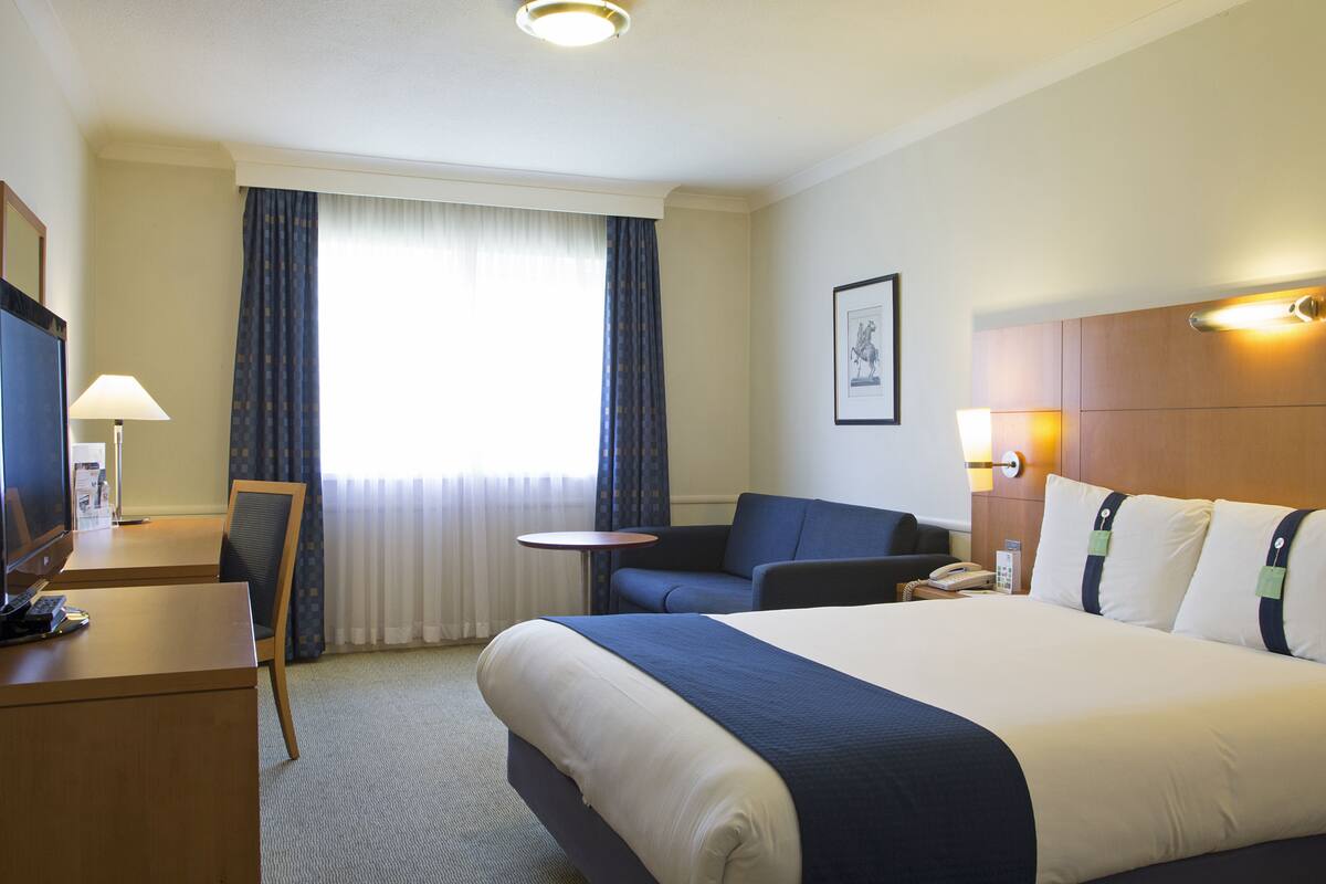 A hotel room with a large bed, a desk with a chair, a small table, and a sofa.