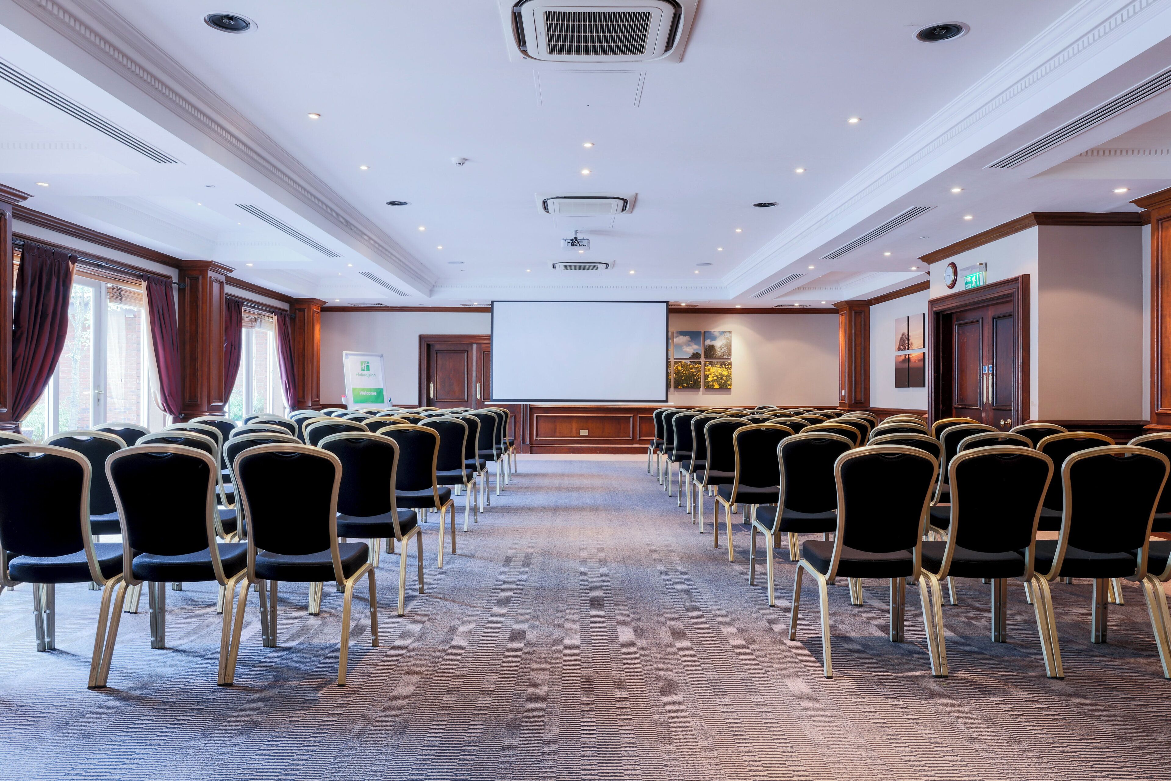 A conference room with rows of chairs, a projector screen, and a presentation area.