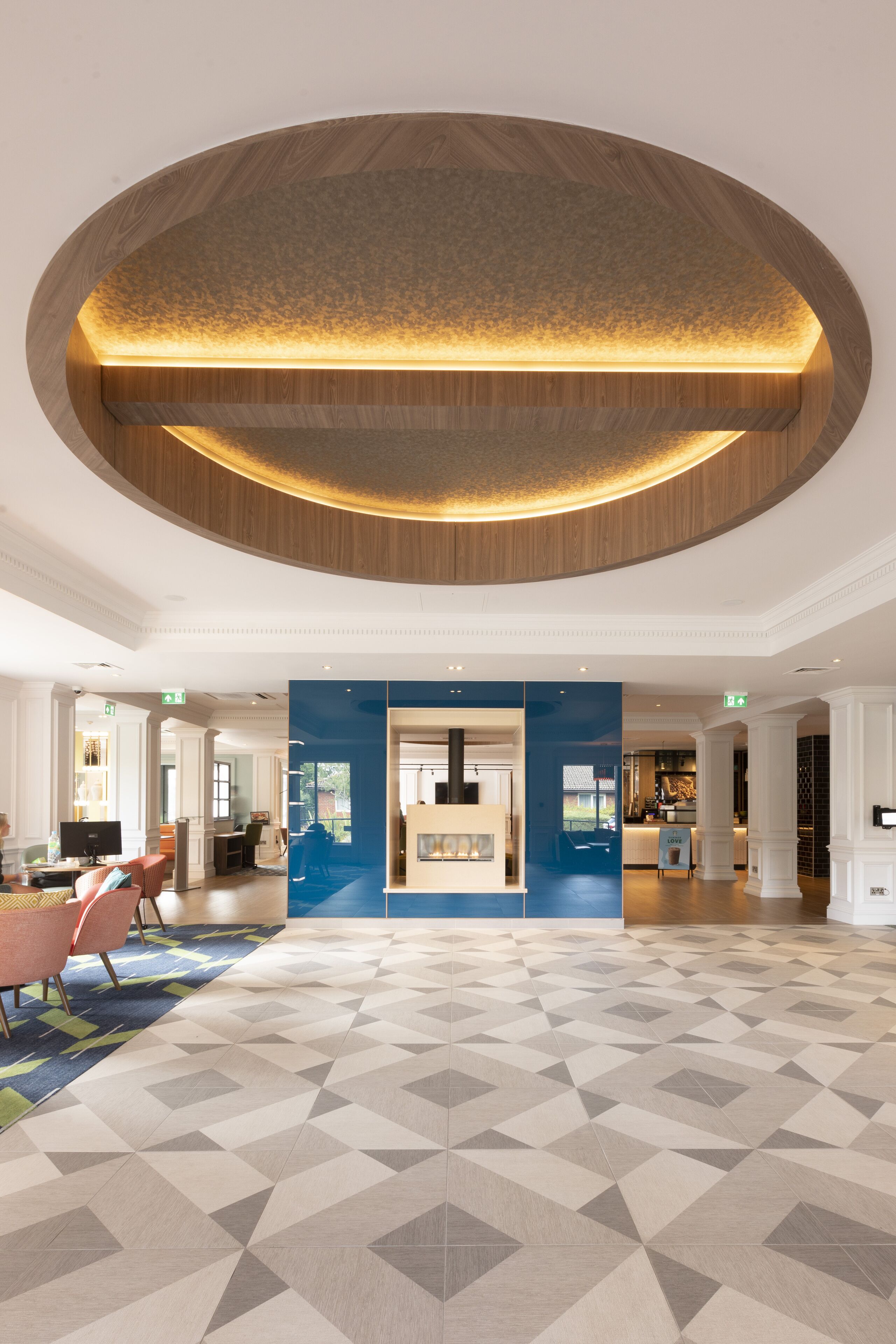 A spacious lobby with a geometric patterned floor, a central reception desk, and a wooden ceiling feature.