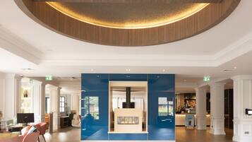 A spacious lobby with a geometric patterned floor, a central reception desk, and a wooden ceiling feature.