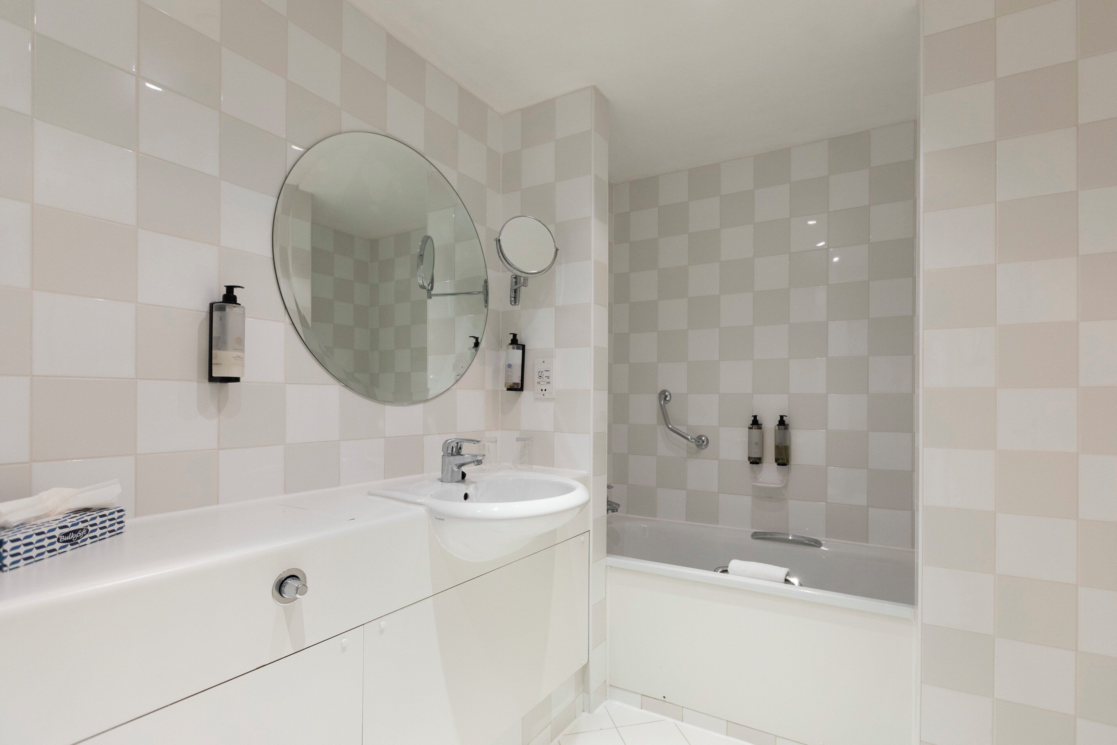 A modern bathroom with a large mirror, a sink, and a bathtub.