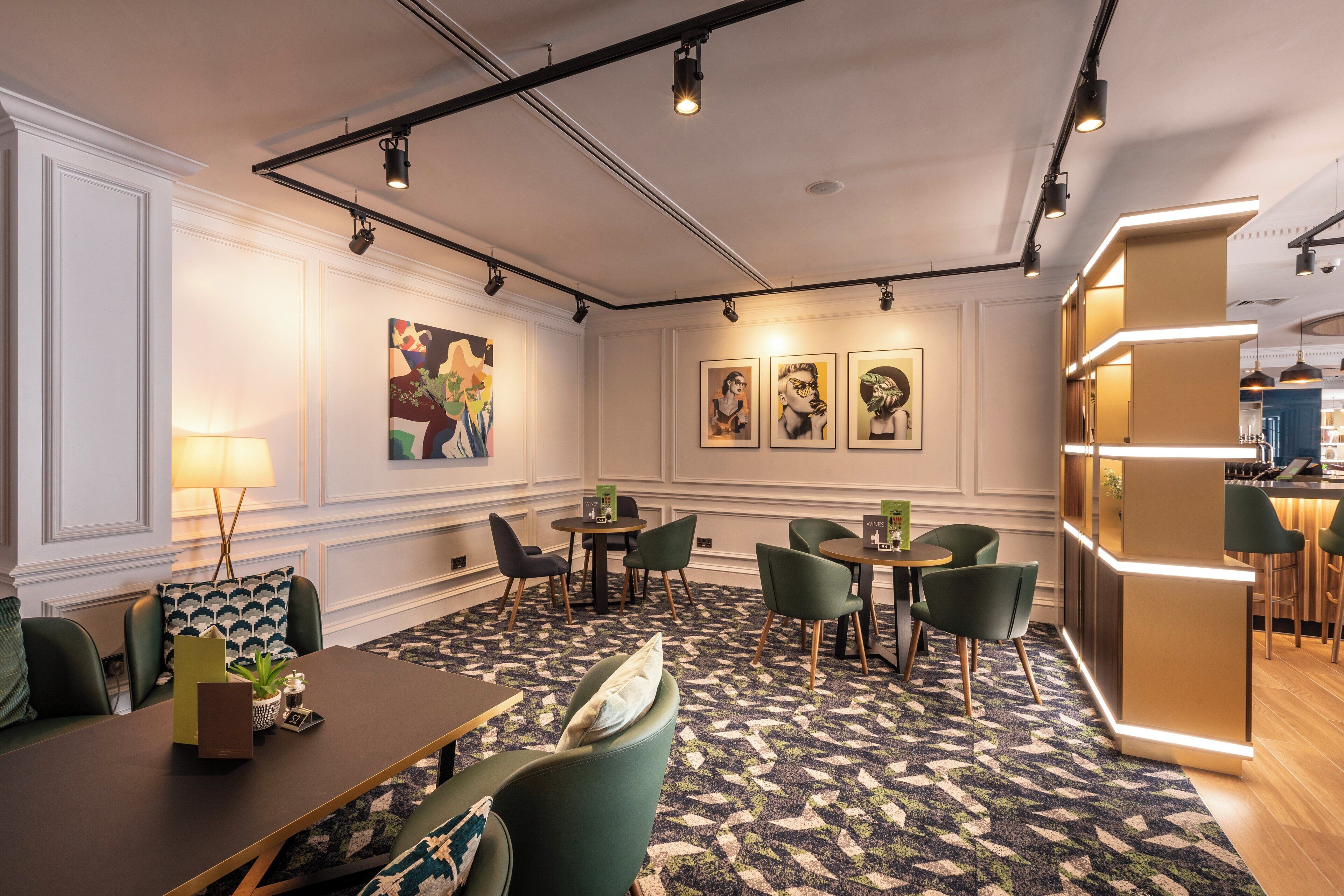 Eine moderne Hotelhalle mit einer zentralen Sitzgelegenheit, Tischen, Stühlen und Kunstwerken an den Wänden.