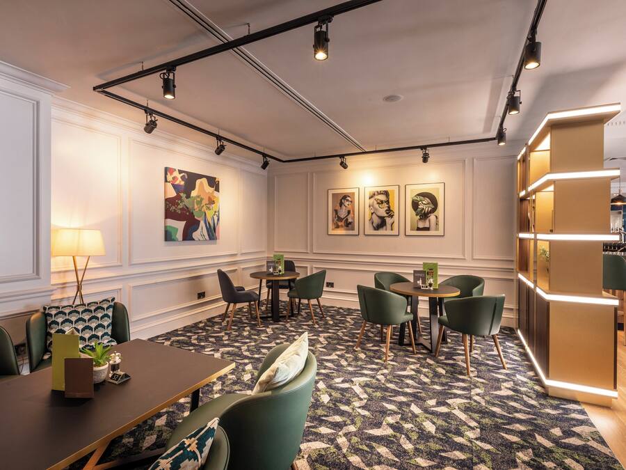 A modern hotel lobby with a central seating area, tables, chairs, and artwork on the walls.