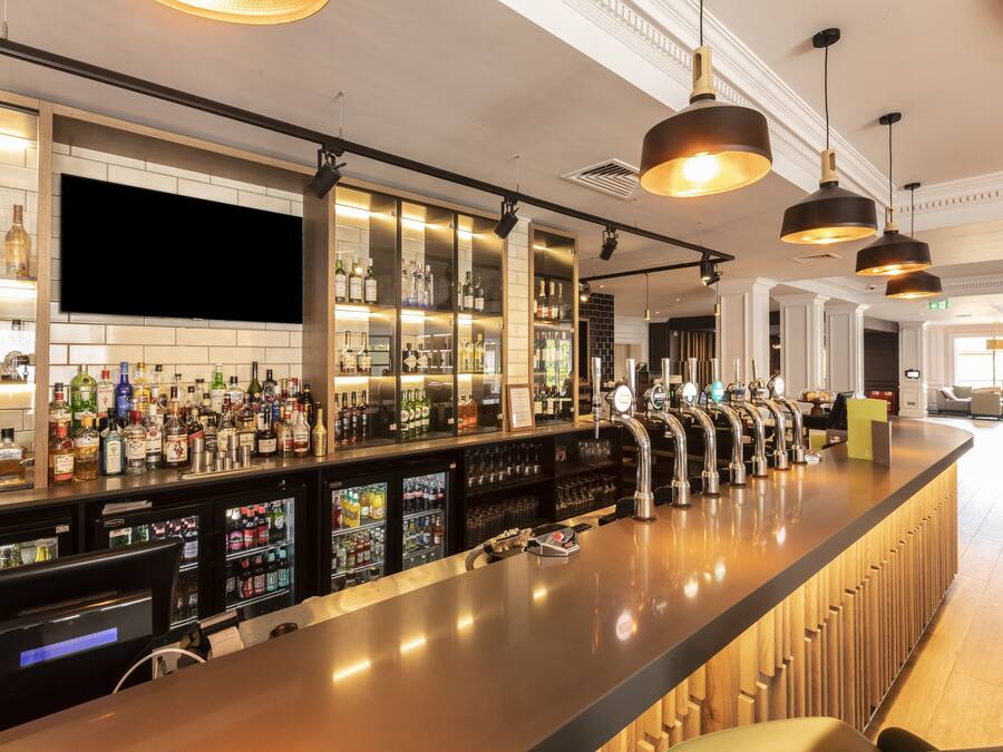 Um bar moderno com um balcão comprido, várias torneiras e uma variedade de garrafas e copos.