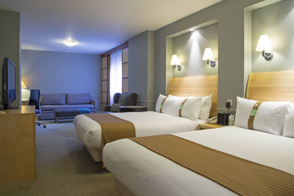 A hotel room with two beds, a sofa, a desk, and a television.