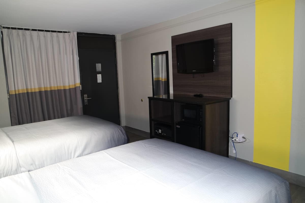 A hotel room with two beds, a TV mounted on the wall, and a desk with a mirror.