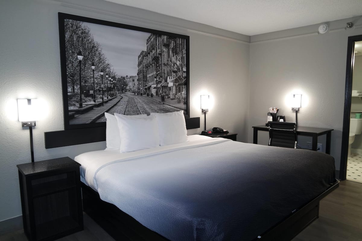 A hotel room with a large bed, two bedside tables, a nightstand, a desk, and a chair.