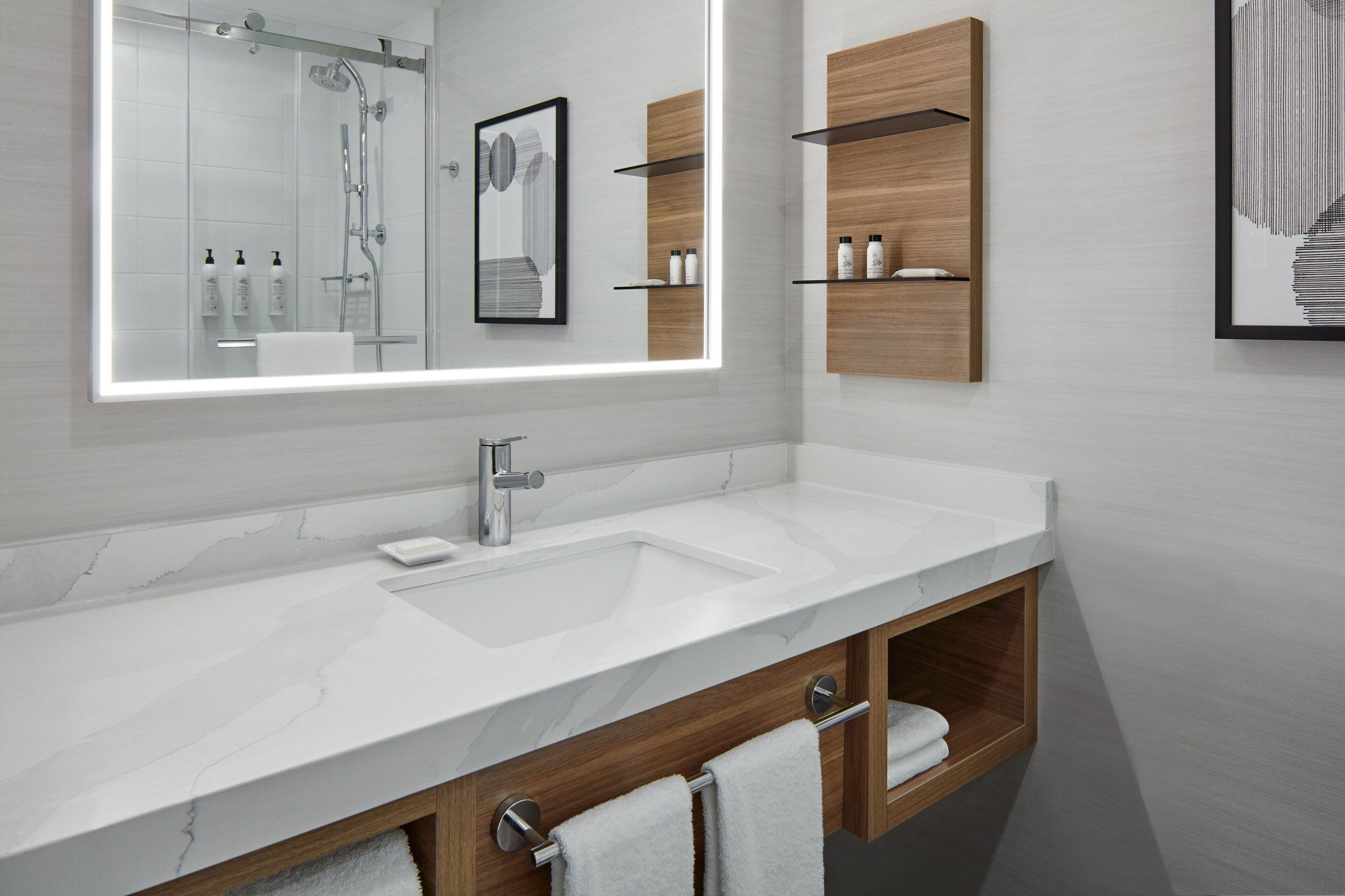 A modern bathroom with a large mirror, two sinks, wooden cabinets, and a shower area.