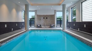 A modern indoor swimming pool with two lounge chairs, a tiled wall with a geometric pattern, and large windows. - Delta Hotels by Marriott Toronto Markham (Markham)