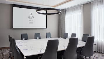 Ein Konferenzraum mit einem langen Tisch, sechs Stühlen und einem großen Bildschirm, der das Delta Hotels Logo zeigt.