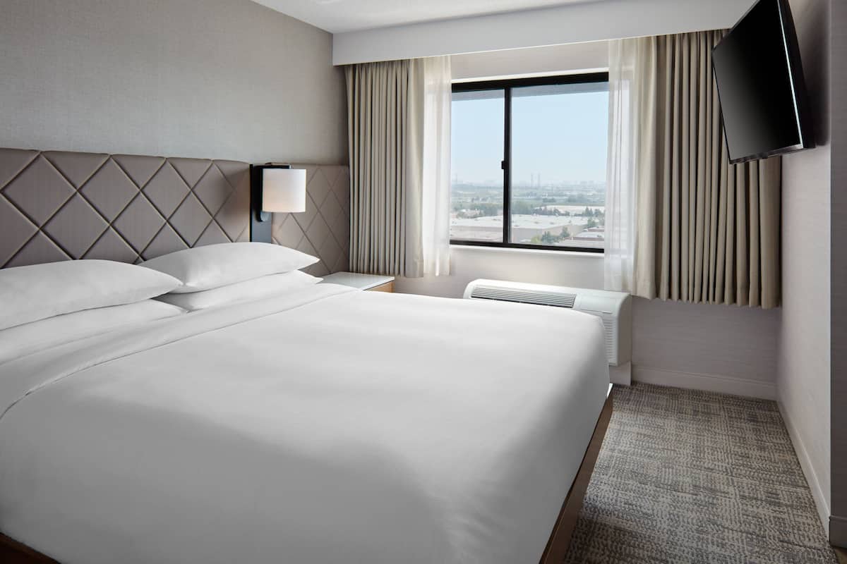 A hotel room with a large bed, a flat-screen TV mounted on the wall, and a window with curtains.