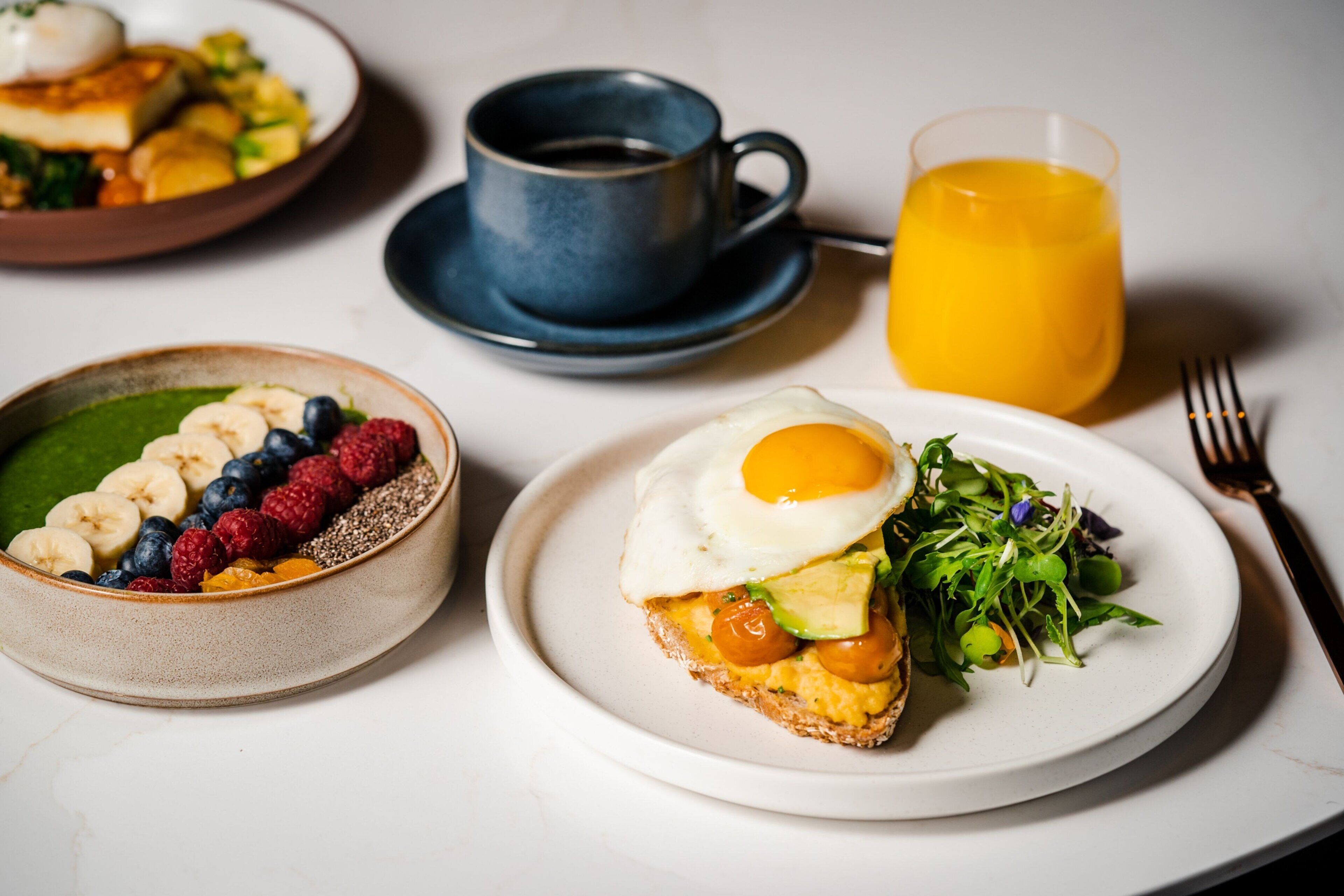 Un desayuno con distintos platos, una taza de café y un vaso de zumo de naranja.