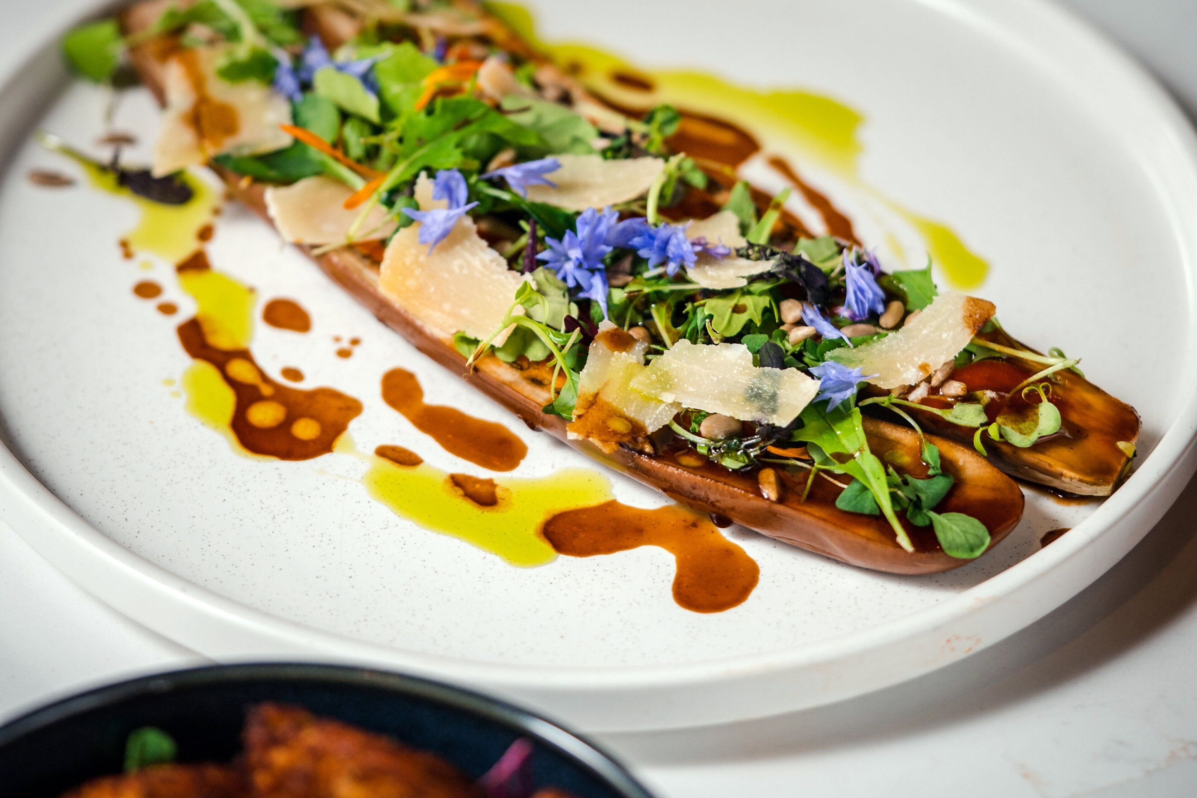 A white plate with a food item topped with greens, cheese, and sauce.