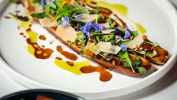 A white plate with a food item topped with greens, cheese, and sauce.
