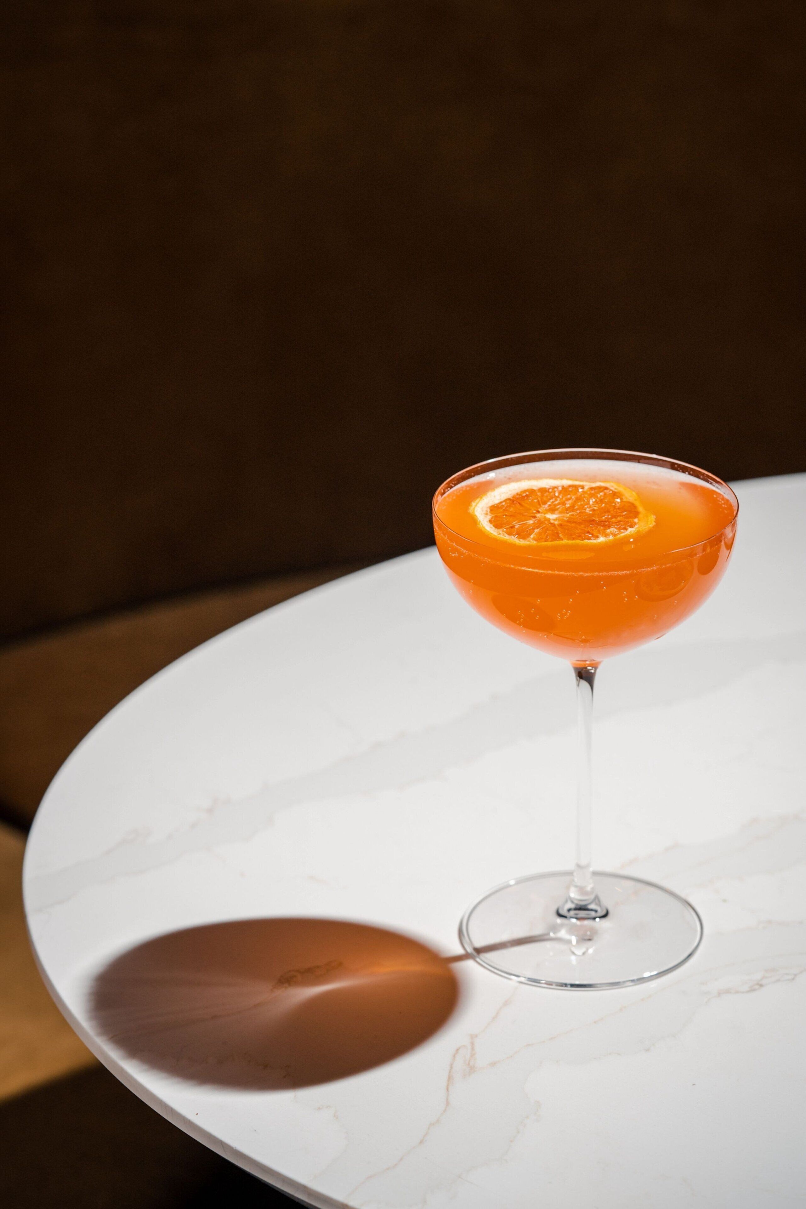 A cocktail in a martini glass on a white marble table.