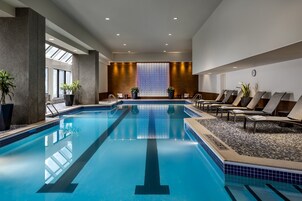 An indoor swimming pool with clear lanes, lounge chairs, and potted plants.