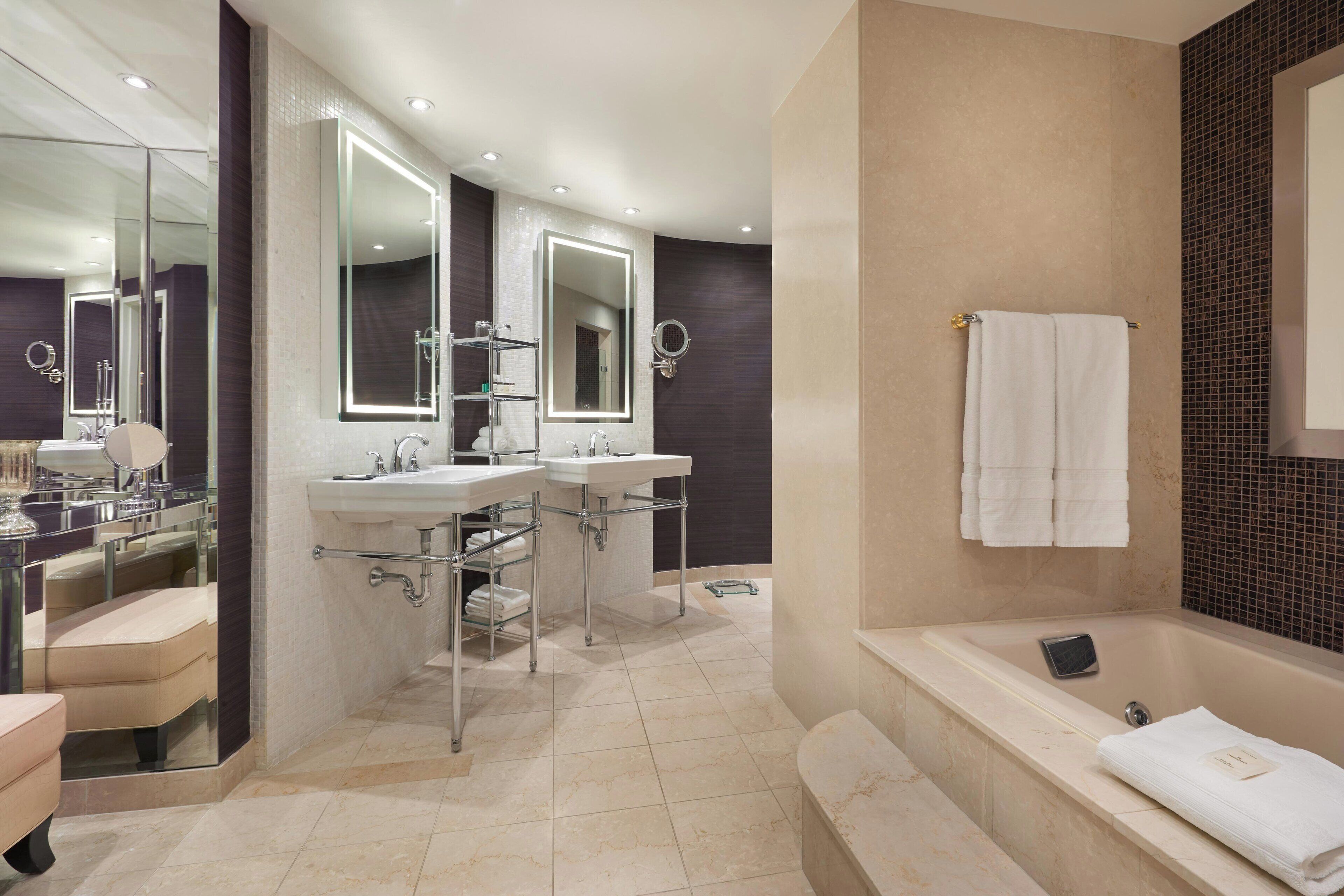 Un baño moderno con dos lavamanos, un espejo grande, una bañera y una zona de ducha con paredes de vidrio.