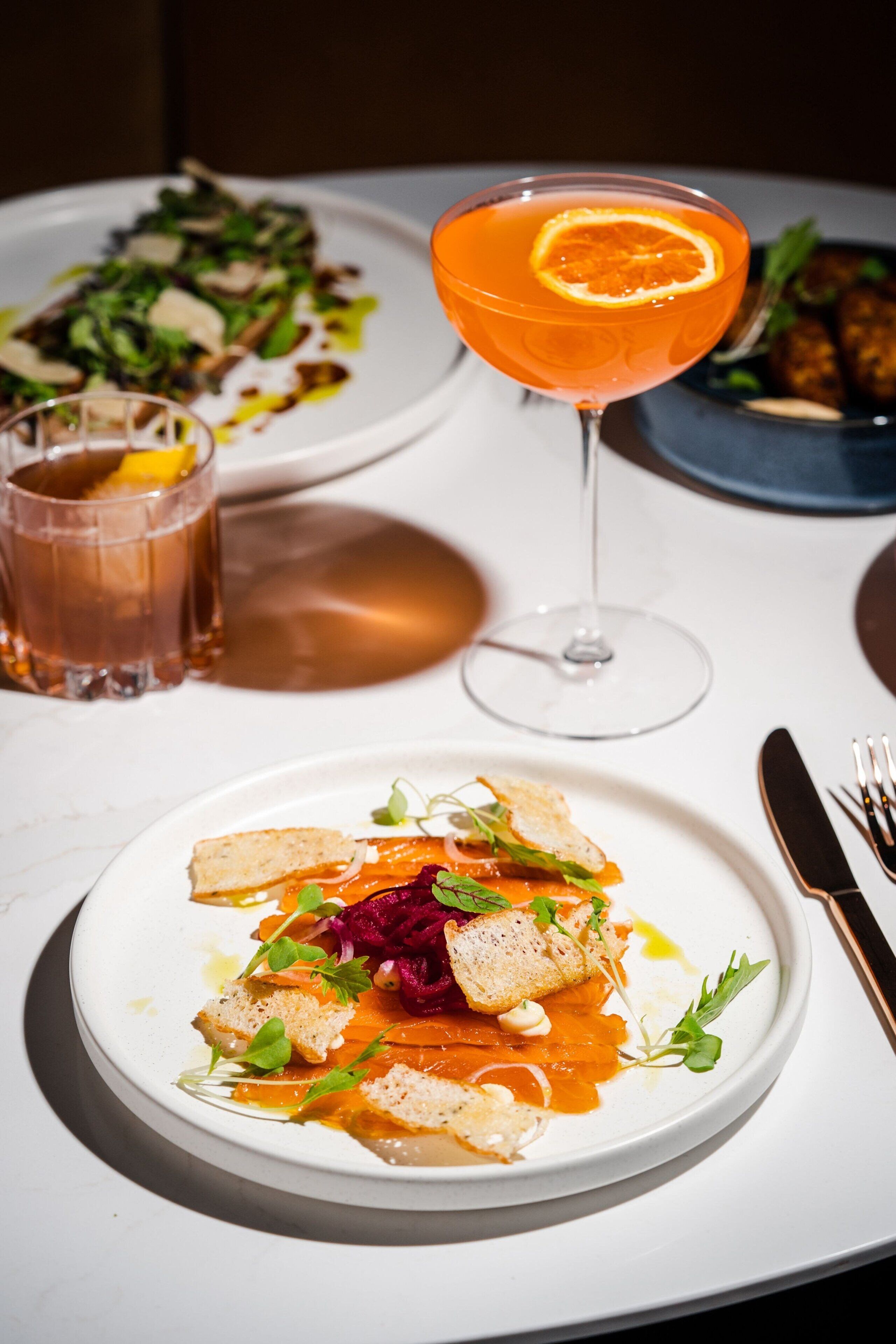 A dining table with a plate of food, a glass of drink, and a fork and knife.