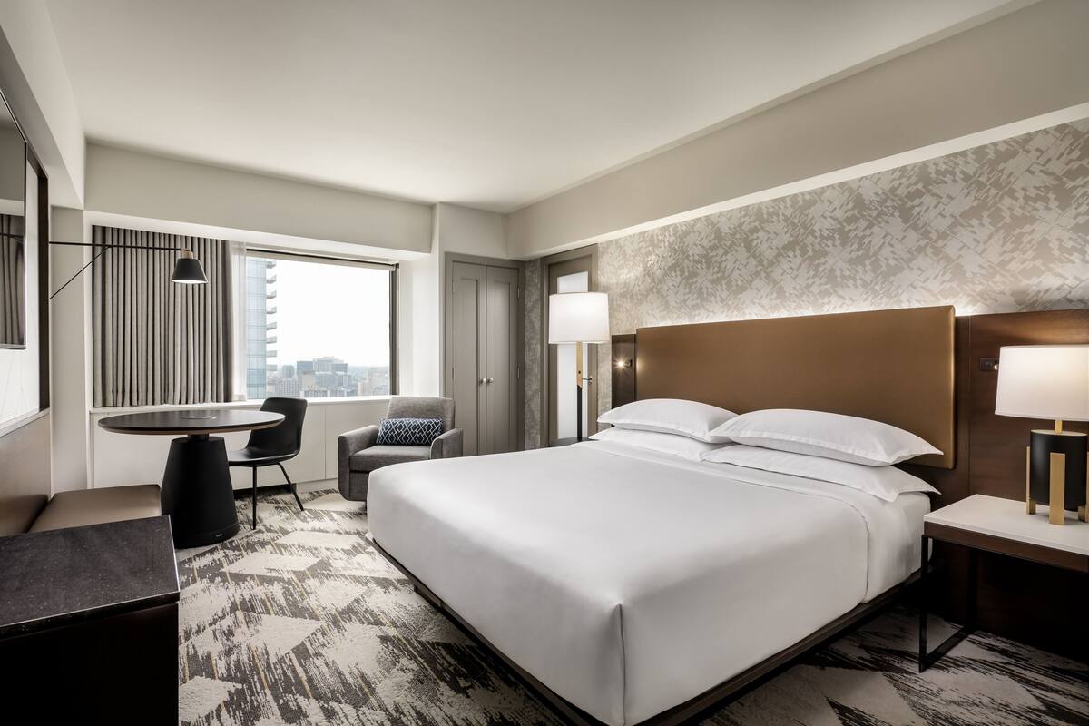 Een hotelkamer met een groot bed, een bureau, een stoel en uitzicht op de stad.
