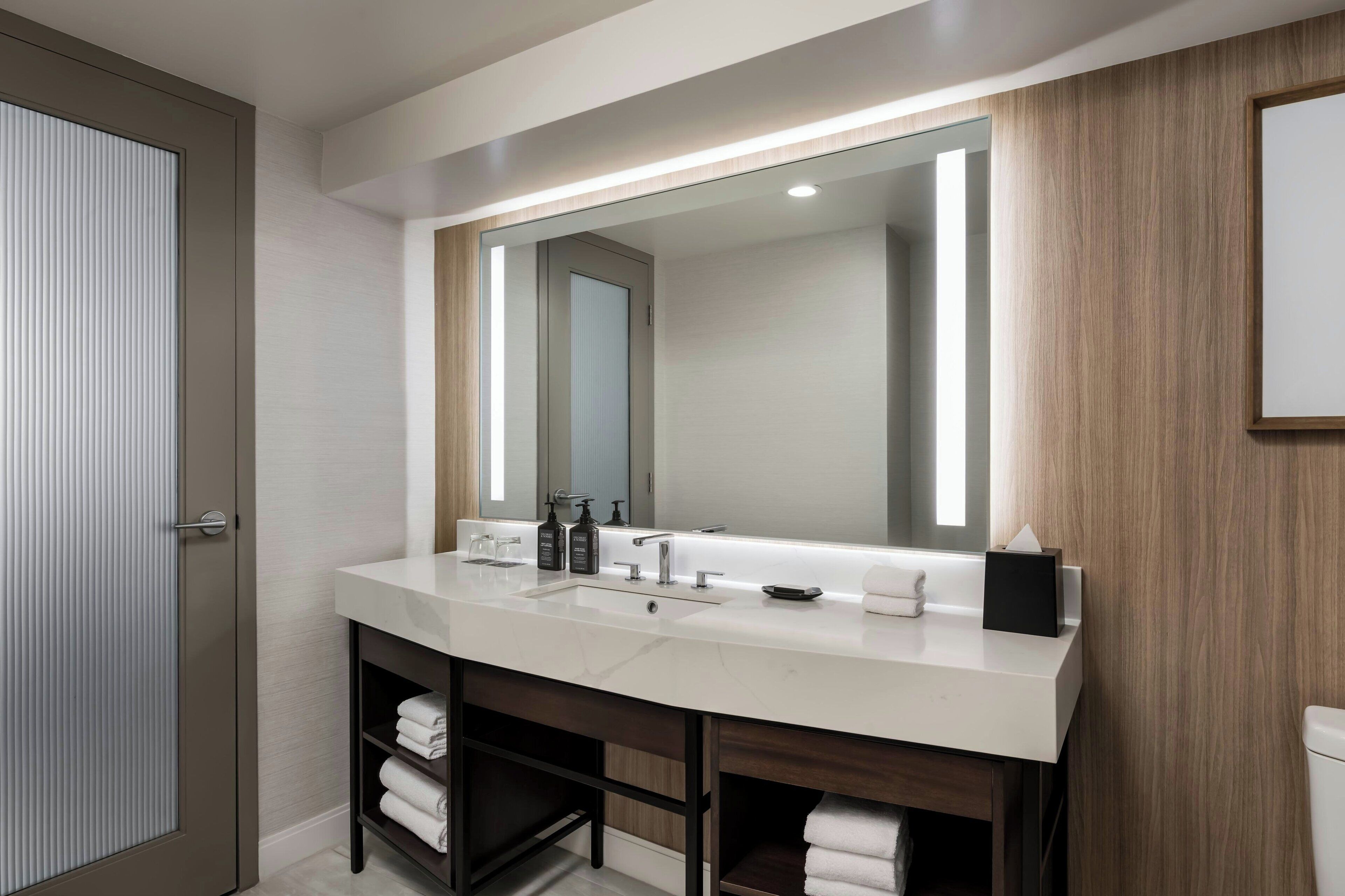 Un baño moderno con un espejo grande, dos lavamanos y un tocador con estantes.