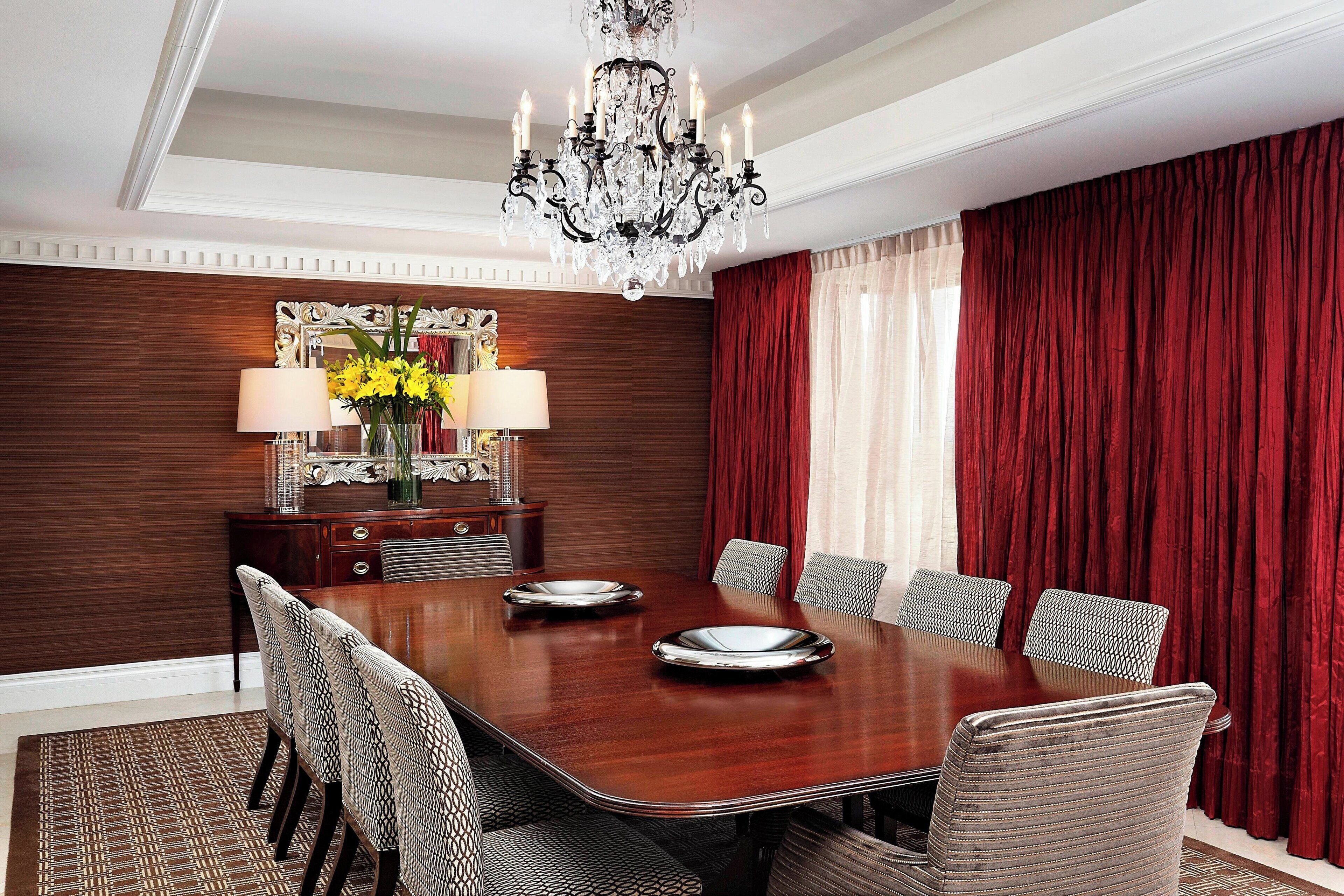 A formal dining room with a large wooden table, six upholstered chairs, a chandelier, and a decorative mirror.