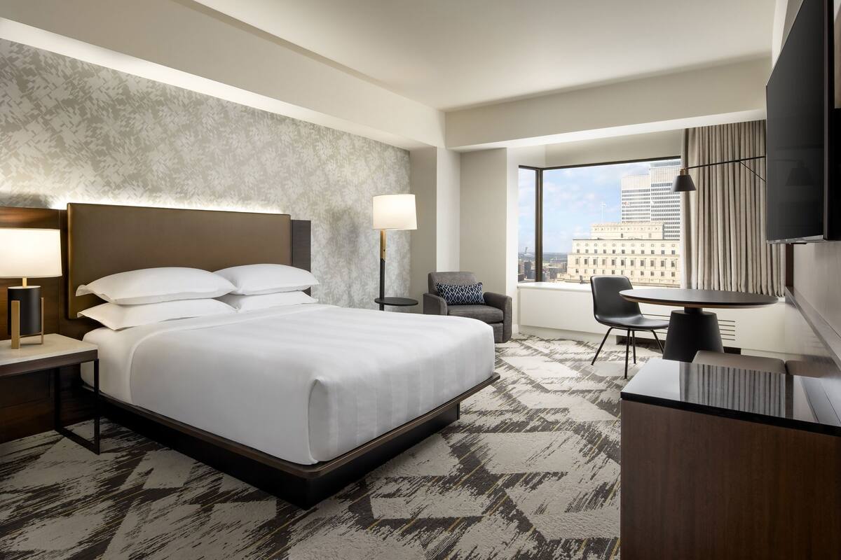 Een hotelkamer met een groot bed, een bureau, een stoel, een televisie en uitzicht op de stad.