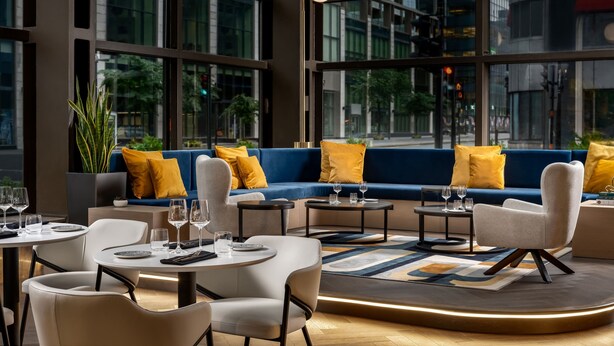 Ein modernes Interieur mit einem blauen Sofa, weißen Stühlen und einem runden Tisch mit Gläsern.