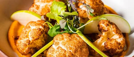 Un tazón de comida con coliflor y vegetales verdes.