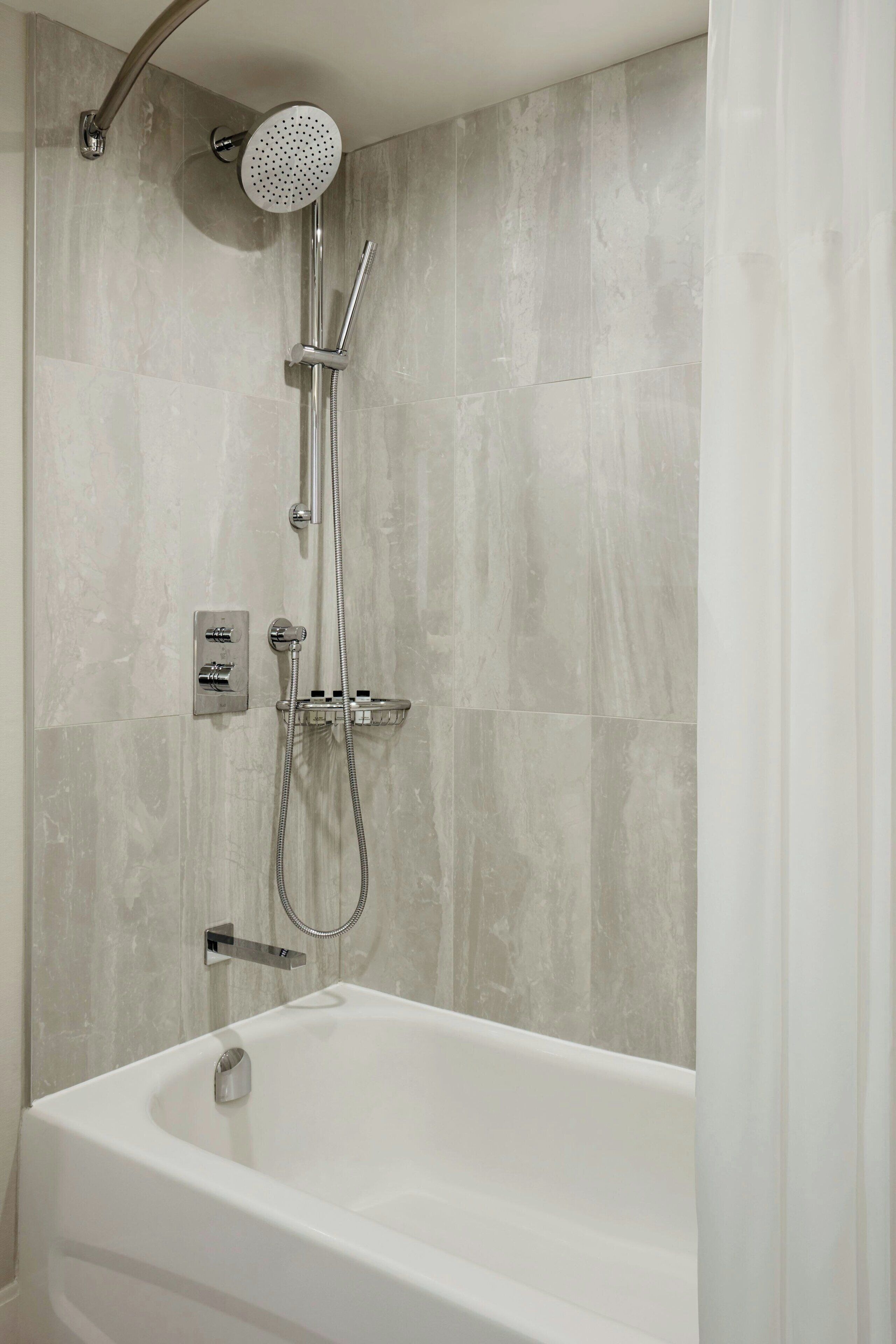 A modern bathroom with a freestanding bathtub, a handheld showerhead, and a wall-mounted control panel.