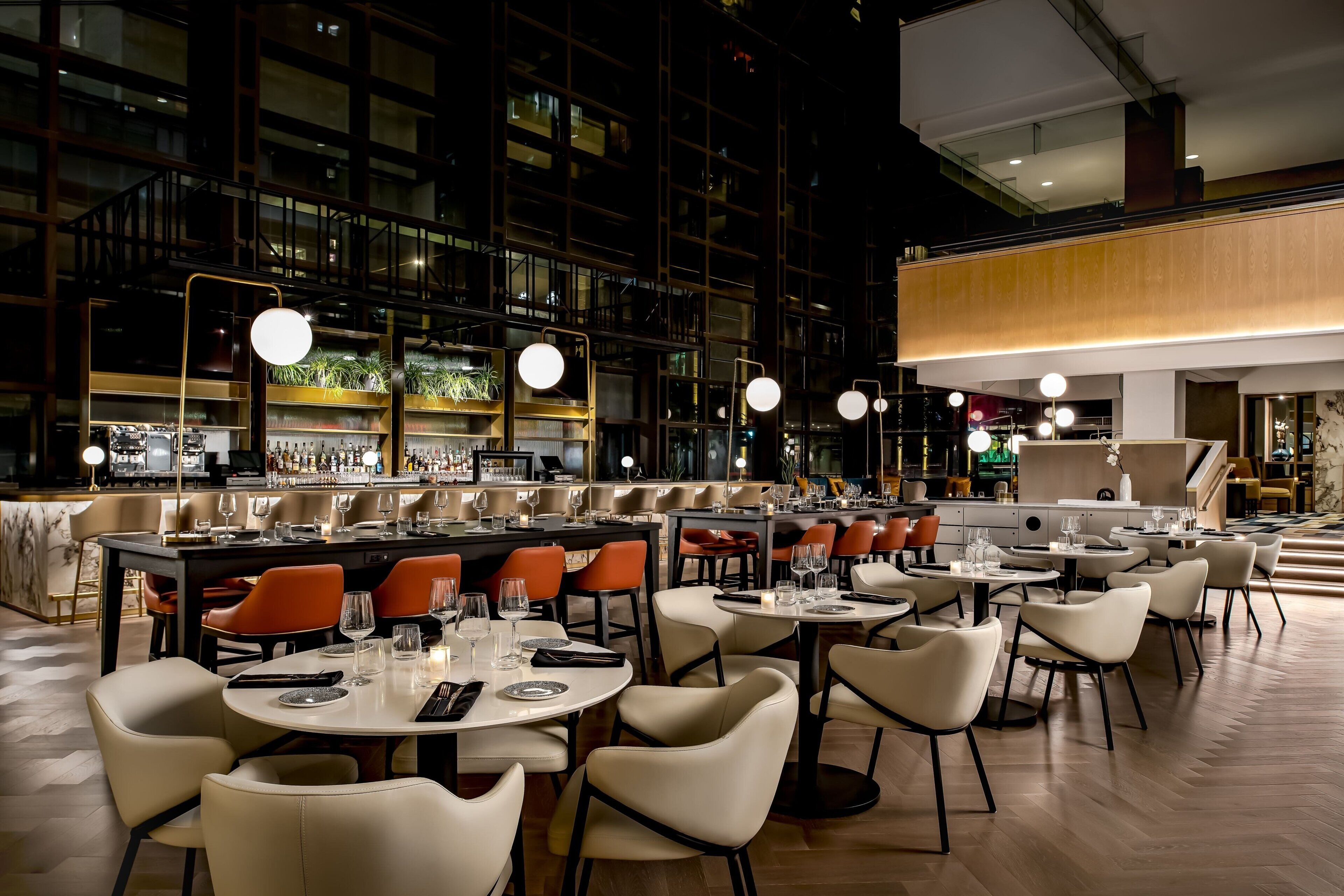 A modern restaurant with multiple dining areas, a bar, and a view of a high-rise building.