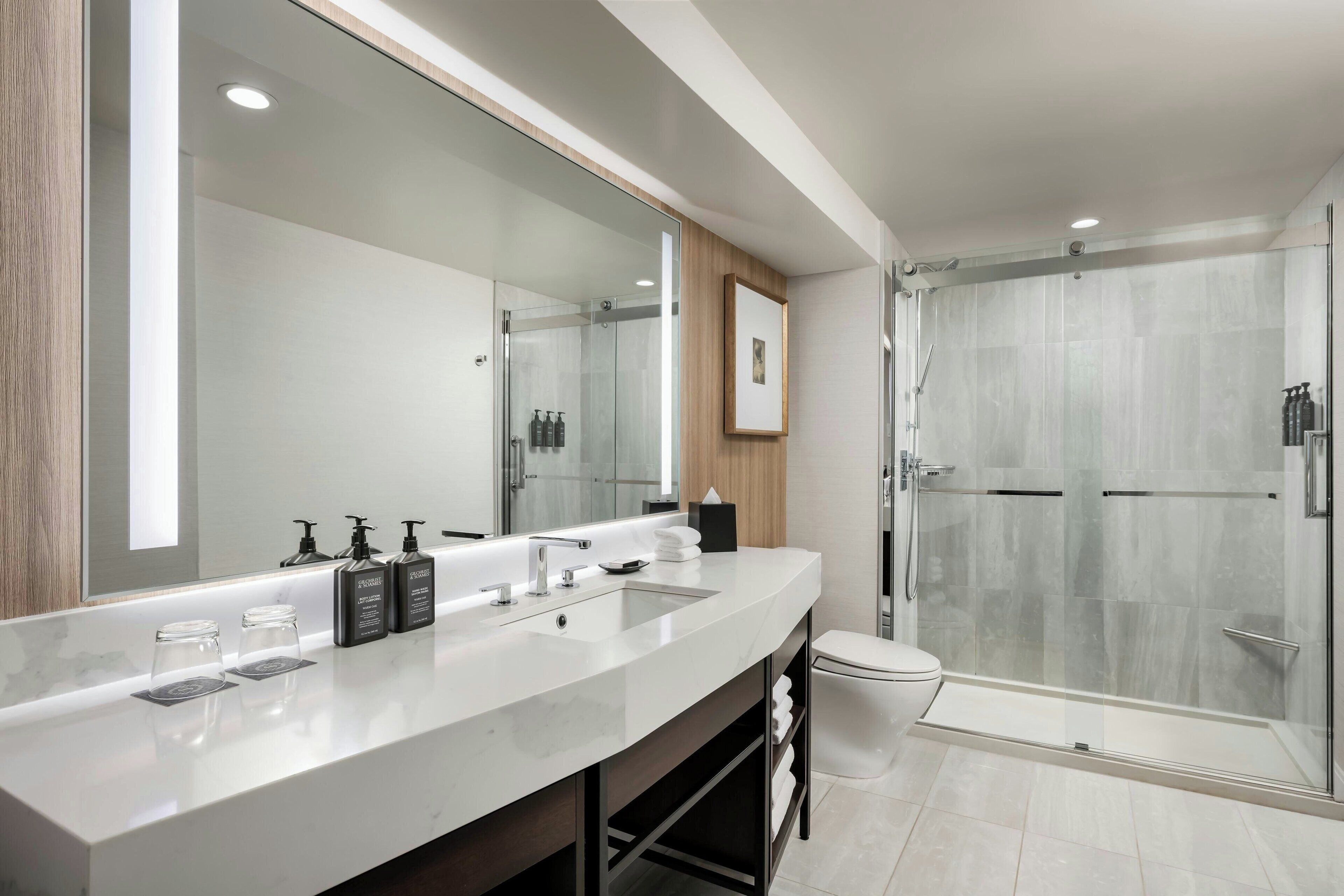 A modern bathroom with a large mirror, a white sink, and a glass-enclosed shower.