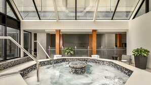 Ein moderner Poolbereich im Innenbereich mit Glasdecke, einer zentralen Whirlwanne und einer Pflanzensitzgruppe.