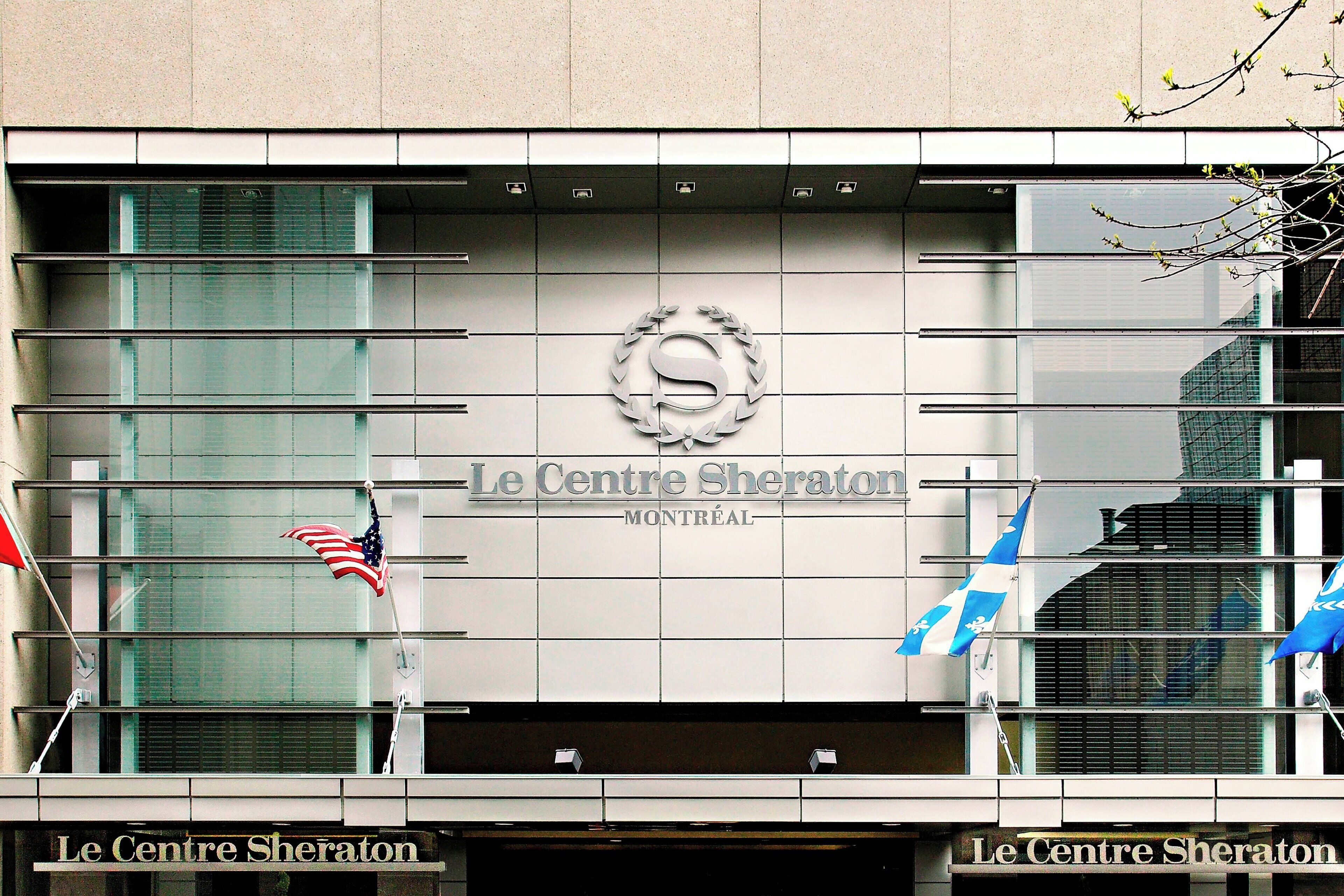 La façade de l’hôtel Le Centre Sheraton à Montréal, avec son logo bien visible, les drapeaux américain et canadien, et son architecture moderne.