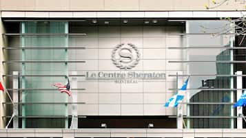 Exterior del Hotel Le Centre Sheraton en Montreal, con un logo destacado, las banderas de Estados Unidos y Canadá, y un diseño arquitectónico moderno.