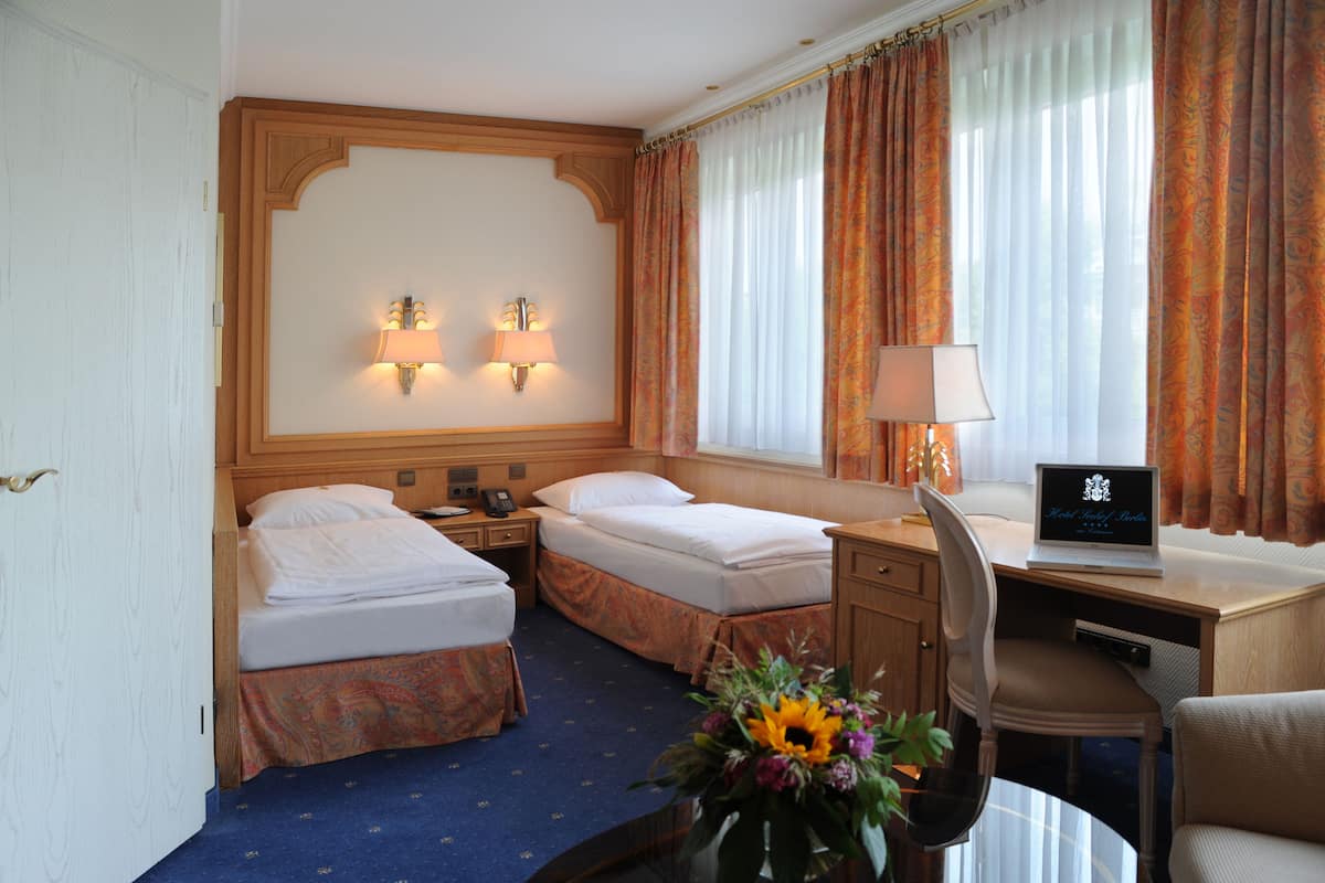 A hotel room with two beds, a desk with a laptop, a chair, a desk lamp, and a vase with flowers.