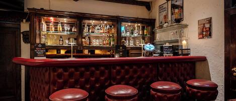 A bar area with a wooden counter, glass display cases, and leather stools.